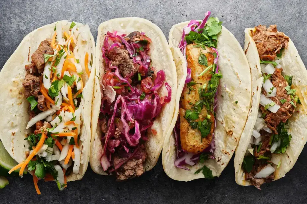 Four assorted Mexican tacos with varied meats and colorful toppings
