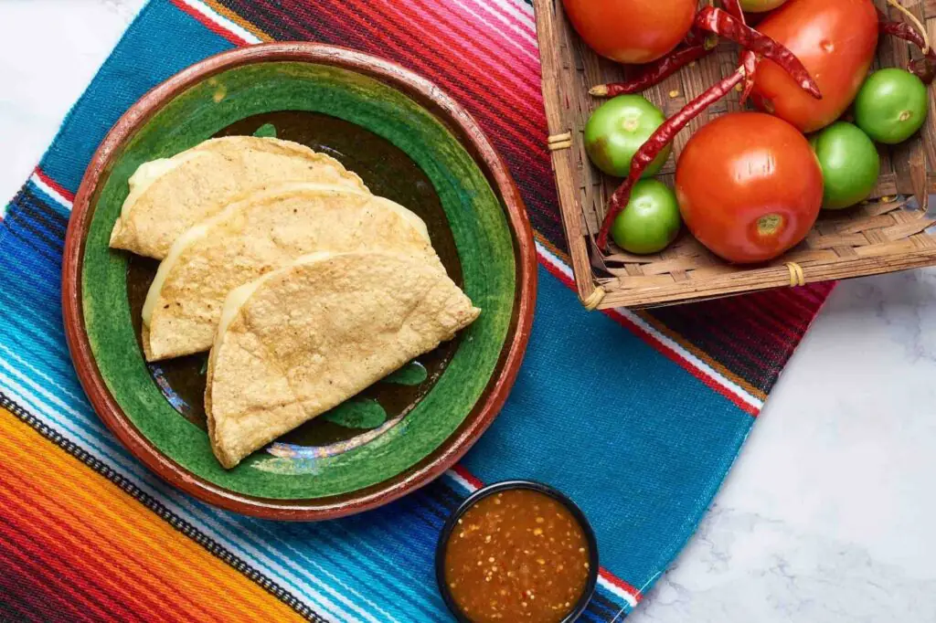 Folded corn taco shells on a plate with salsa and fresh tomatoes