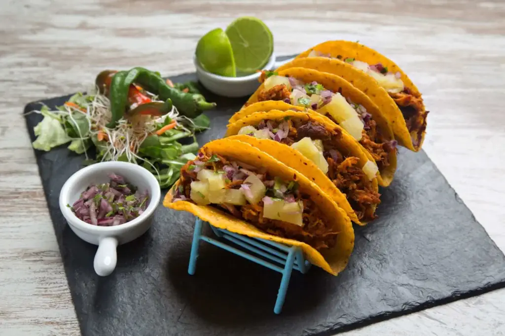 Al pastor tacos with pineapple, diced onion and lime wedge