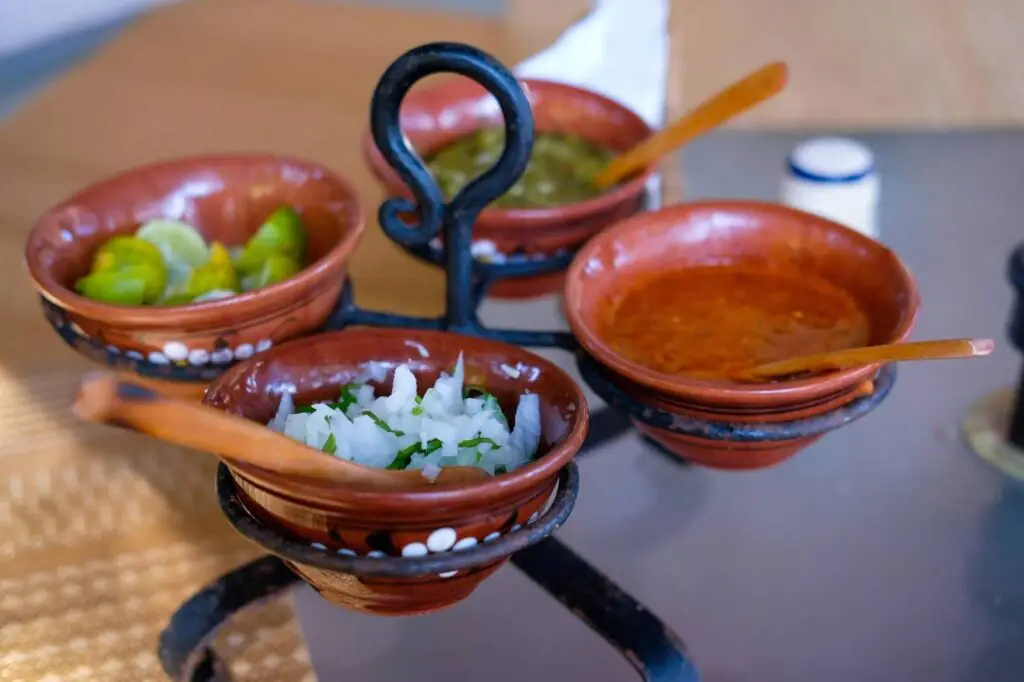 Terracotta bowls on stand with red salsa, green salsa, chopped onion and lime