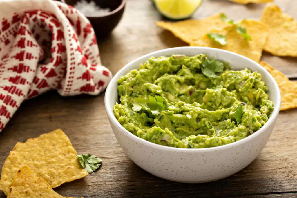Bowl of mashed guacamole garnished with cilantro and tortilla chips