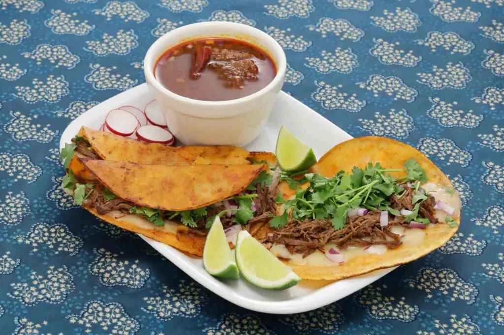 Birria tacos with cilantro, onion, lime and consommé dip
