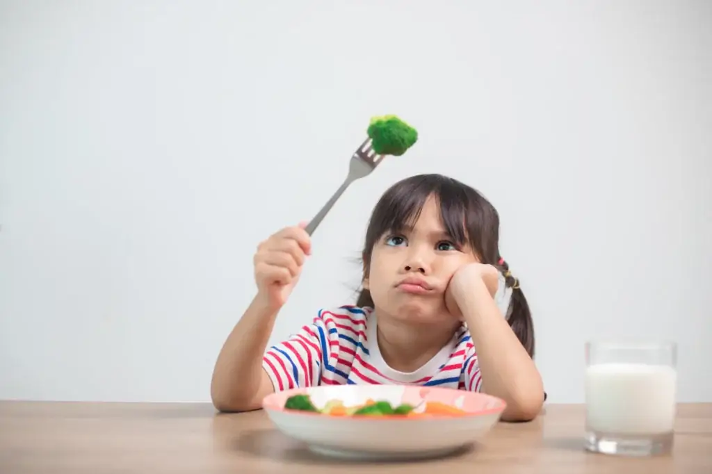 Young girl poking broccoli, looking like a picky eater at dinner